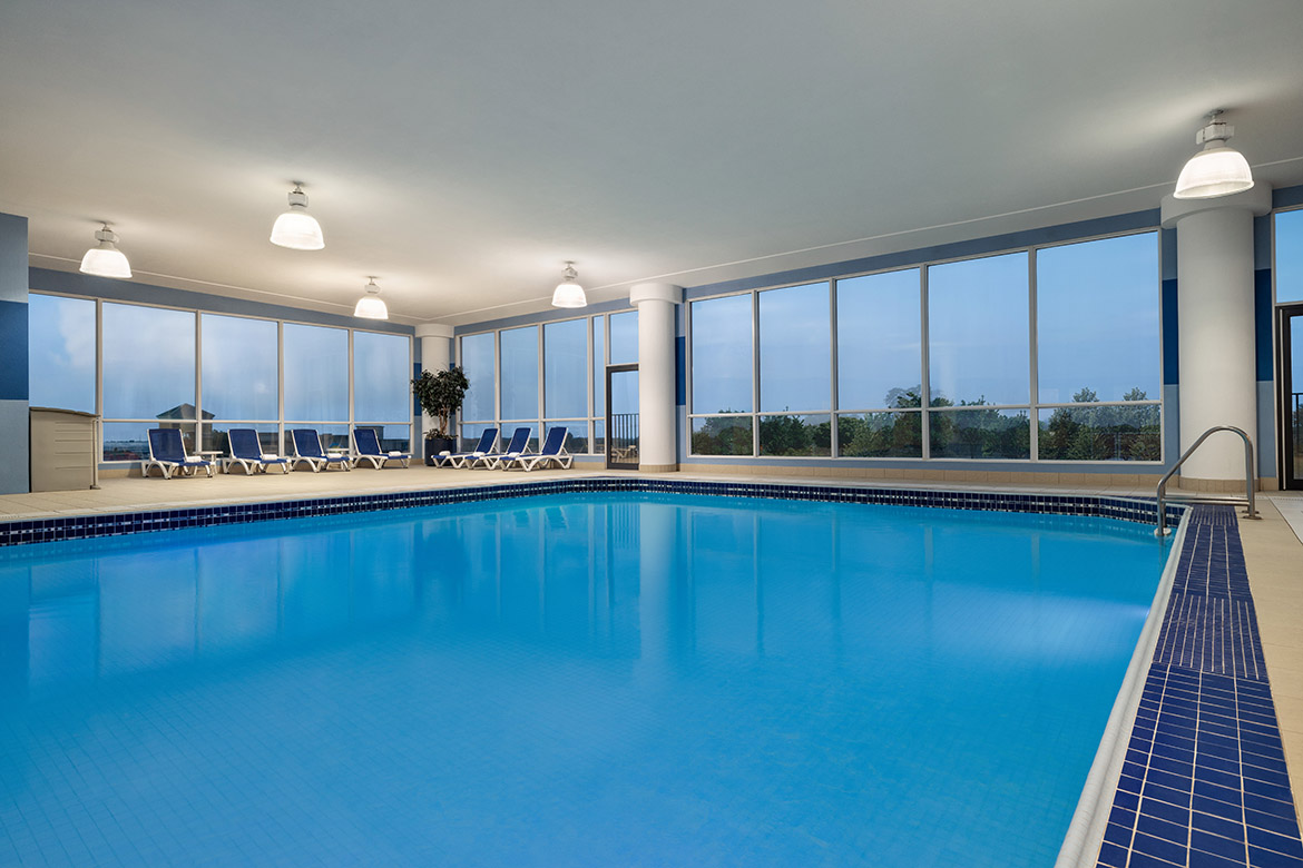 Indoor hotel pool with lounge chairs and full-height windows